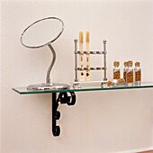 Shaving mirror with toothbrush holder and small bottles on glass shelf
