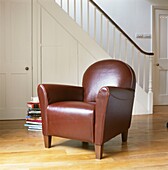 Leather armchair and stack of books in open plan entrance hall with staircase and banister