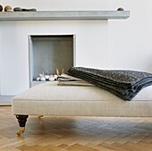 Grey folded fabric on cream chaise longue with caster wheels and contemporary fireplace