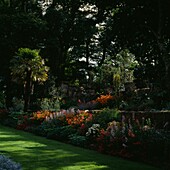Mehrstöckige Blumenbeete mit Palme und Rasen in einem Landschaftsgarten