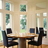 Black leather chairs at contemporary dining table with mirror set in shuttered bay windows