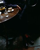 Mann sitzt an einem polierten Holztisch mit Teekanne und Tasse