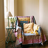 Bunte Patchwork-Decke über einem Sessel in einer Zimmerecke neben dem Erkerfenster