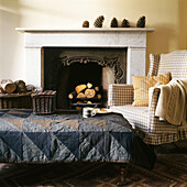 Patchwork tweed covered ottoman in front of fireplace with checked armchair
