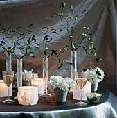 White Christmas party decorations with mistletoe and frosted glass candle holders on silver tablecloth