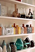 Reihen von Glas-Sammelvasen und -flaschen auf einem offenen Regal in einem Wohnzimmer