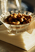 Glass dish filled with cashew nuts on pile of napkins on bar counter