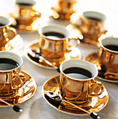 Goldene Tassen mit gewürztem Kaffee und in dunkle Schokolade getauchte Löffel