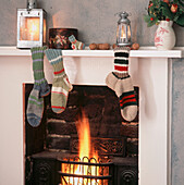 Weihnachten in einem Cottage mit handgestrickten gestreiften Socken auf dem Kaminsims über dem offenen Feuer