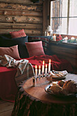 Beleuchtete Kerzen auf einem Tisch aus massivem Kiefernstamm im Wohnzimmer eines Holzchalets