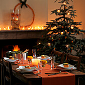 Weihnachtlich gedeckter Tisch in Orangetönen mit offenem Feuer und flackernden Kerzen