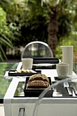 Gedeckter Tisch im Garten mit schwarz-weißem Geschirr, Brot und Plexiglasstühlen