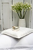 Silberne Deckeldose auf einem weißen Kissen mit einer Vase mit Agapanthus-Blüten im Hintergrund