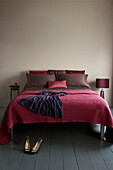 Blick auf ein Doppelbett mit Satinbettwäsche und Überwurf mit lila Seidenkleid und High Heels