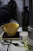 Yellow teacup with black notebook  bottle and scented candle on bedside table