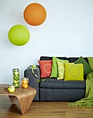 Bright orange and green pendant lights above grey sofa with upholstered cushions