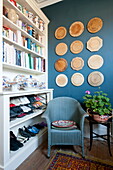 Blue chair in front of storage shelves with decorative wall mounted plaques in Greenwich home,  London,  England,  UK