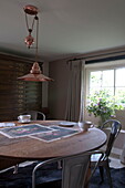 Runder Esstisch aus Holz mit Metallstühlen unter einer Pendelleuchte aus Messing Kingston home, East Sussex, England, UK