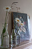 Cut daisies in bottles with artwork on mantlepiece in Kingston home,  East Sussex,  England,  UK