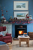 Sessel am Kamin mit Weihnachtsschmuck im blauen Wohnzimmer des Bauernhauses in Tiverton, Devon UK