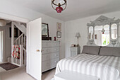 Salvaged mirror above striped bed cover with painted chest and view to landing hallway in Dorset home  Kent  UK