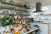 Crockery and glassware on open shelving with cakes and fruit in London home  England  UK