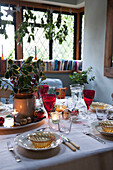 Place setting with coloured glassware and holly on table in Kilndown cottage  Kent  England  UK