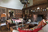 Wandbehänge und Sofas mit Ornamenten am geschnitzten Kamin in einem Haus in Suffolk, England, UK