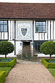 Timber framed exterior of Suffolk house with peacock on gravel footpath  UK
