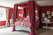 Red fabric four poster bed with silver metallic lampshades in Suffolk farmhouse  England  UK