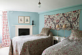 Twin beds with floral covers and wall hanging in light blue Suffolk farmhouse  England  UK