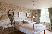 Pair of mirrors and lamps above antique bed in sunlit Suffolk bedroom  England  UK