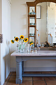 Sonnenblumen und Tassen auf einem Tisch mit Spiegel in einer umgebauten Scheune in Norfolk aus dem 18
