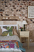 Patchwork auf einem Doppelbett mit freiliegender Steinwand in einer umgebauten Scheune in Norfolk aus dem 18