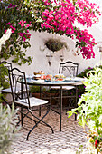 Pink Bougainvillea above wrought iron table and chairs in Castro Marim courtyard, Portugal