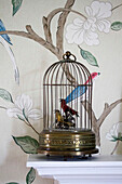 Vogelkäfig auf dem Kaminsims mit gemusterter Tapete in einem Haus in Amberley, West Sussex, England, UK