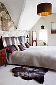 Fur rug at bed with curved wooden headboard in Amberley home West Sussex England UK