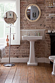Pedestal basin and mirrors at window in exposed brick bathroom of Brighton home, East Sussex, England, UK