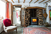 Lit wood-burning stove and firewood stacked in Devon cottage England UK