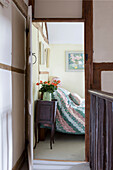 Roses on bedside cabinet seen through bedroom door in Amberley cottage West Sussex UK