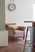 Brown leather armchair below clock in brick floored Petworth farmhouse West Sussex Kent