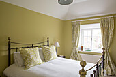 Brass bed at window with co-ordinating muted green walls and fabrics in Petworth farmhouse West Sussex Kent
