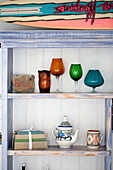 Glassware and books on stripped back shelving in renovated 1950s coastal beach house West Sussex UK