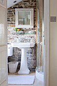 Exposed stone wall with square mirror above pedestal basin in renovated 16th century Rectory house Cornwall UK
