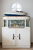 Model boat on vintage cabinet with porthole window in West Wittering home West Sussex England