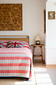Striped bed cover and woodblock artwork with side table in West Wittering home West Sussex England