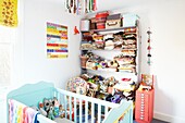 Clothes folded on shelf in child's nursery with turquoise painted cot,  London family home,  England,  UK