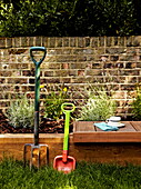 Gartengabel und Kinderspaten neben einem Hochbeet im Außenbereich eines Londoner Einfamilienhauses England UK