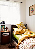 Gardinen und Einzelbett mit gelber Bettdecke und Kissen in einem Haus in Birmingham, England, UK