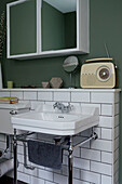 Wall mounted mirrored cabinet with vintage radio in white tiled bathroom of contemporary London home   England   UK